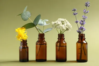 Cztery brązowe butelki z kwiatami: żółtymi, eukaliptusem, białymi i lawendą.