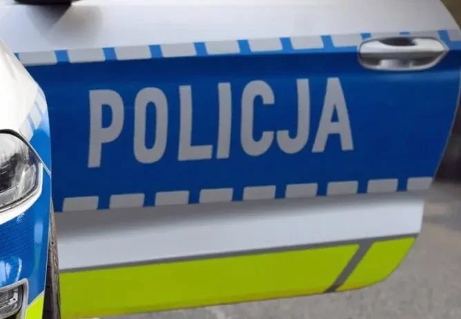 Fragment policyjnego radiowozu z napisem POLICJA na drzwiach.